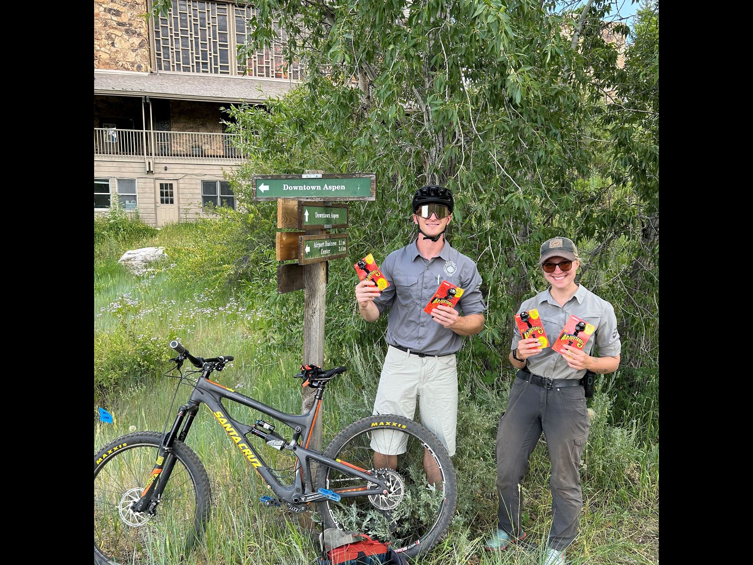 two parks and open space employees standing next to bikes and holding bike bells
