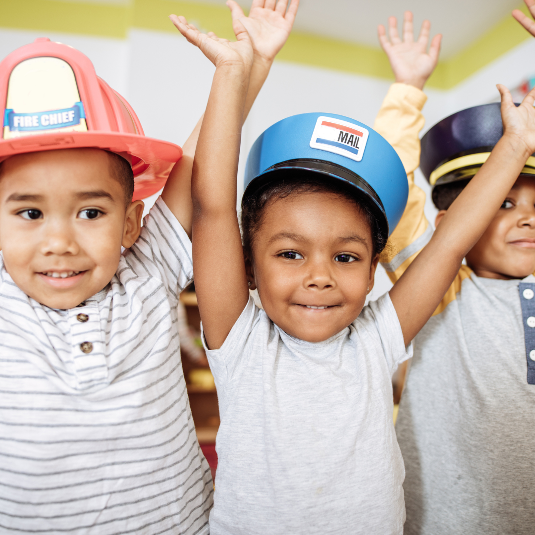 Three young children playing dress up. A fireman, a mailman, and a policeman