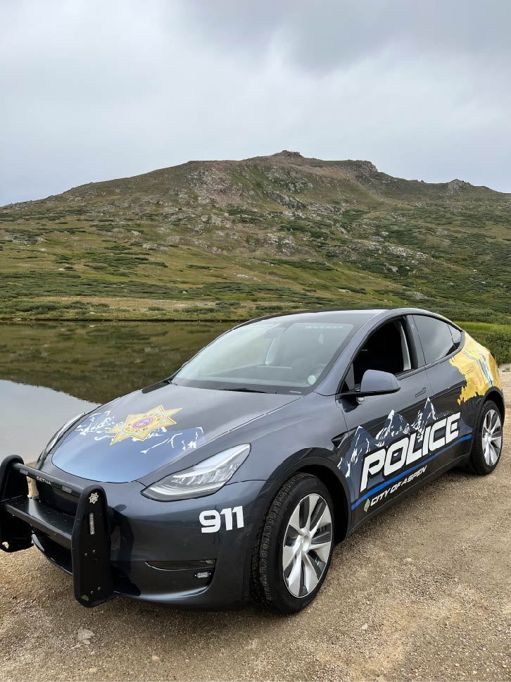 photo of blue tesla with aspen police department logo in front of a green mountain 